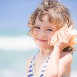 Child holds seashell to her ear